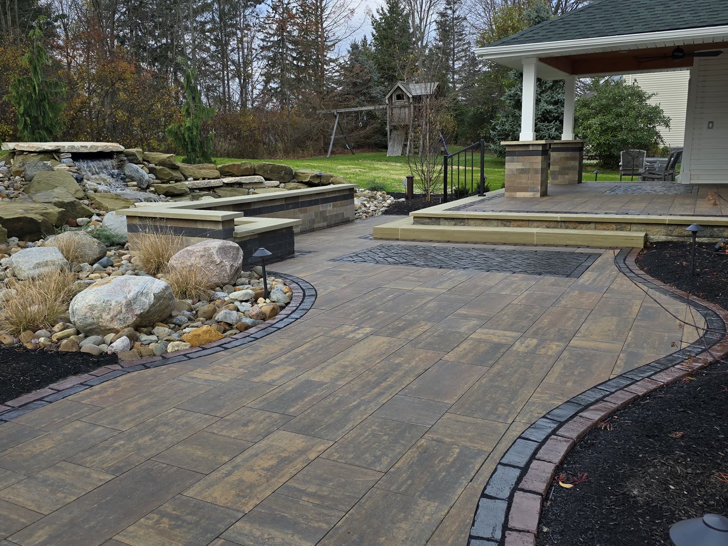 Curved paver backyard with layered walls and landscaped edges