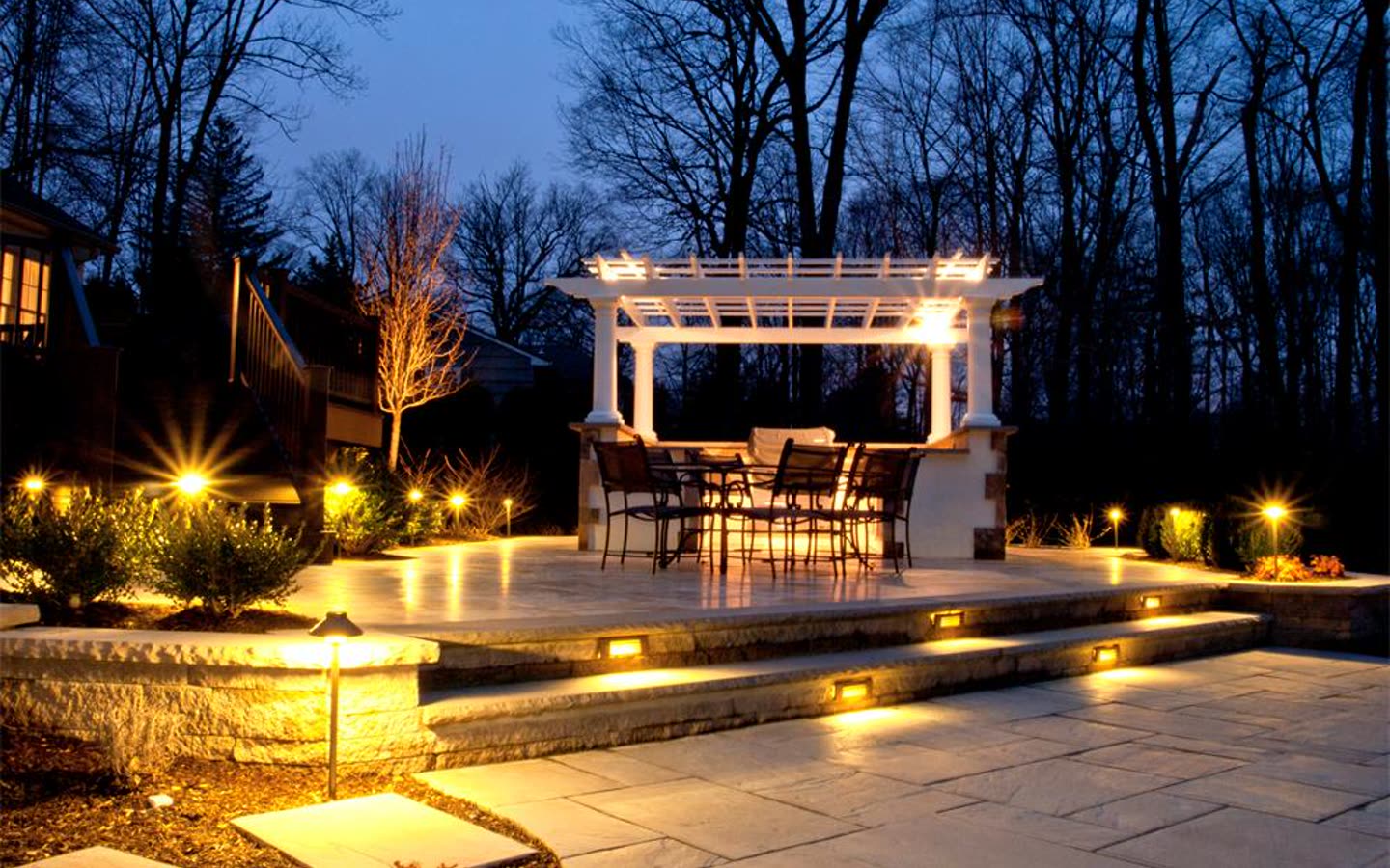 Pergola, patio, and walkway illuminated with warm landscape lighting