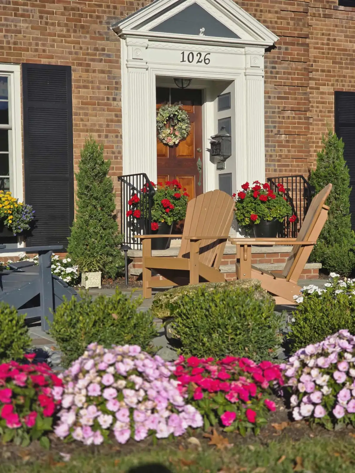 Brick colonial front yard with Adirondack chairs and flower beds